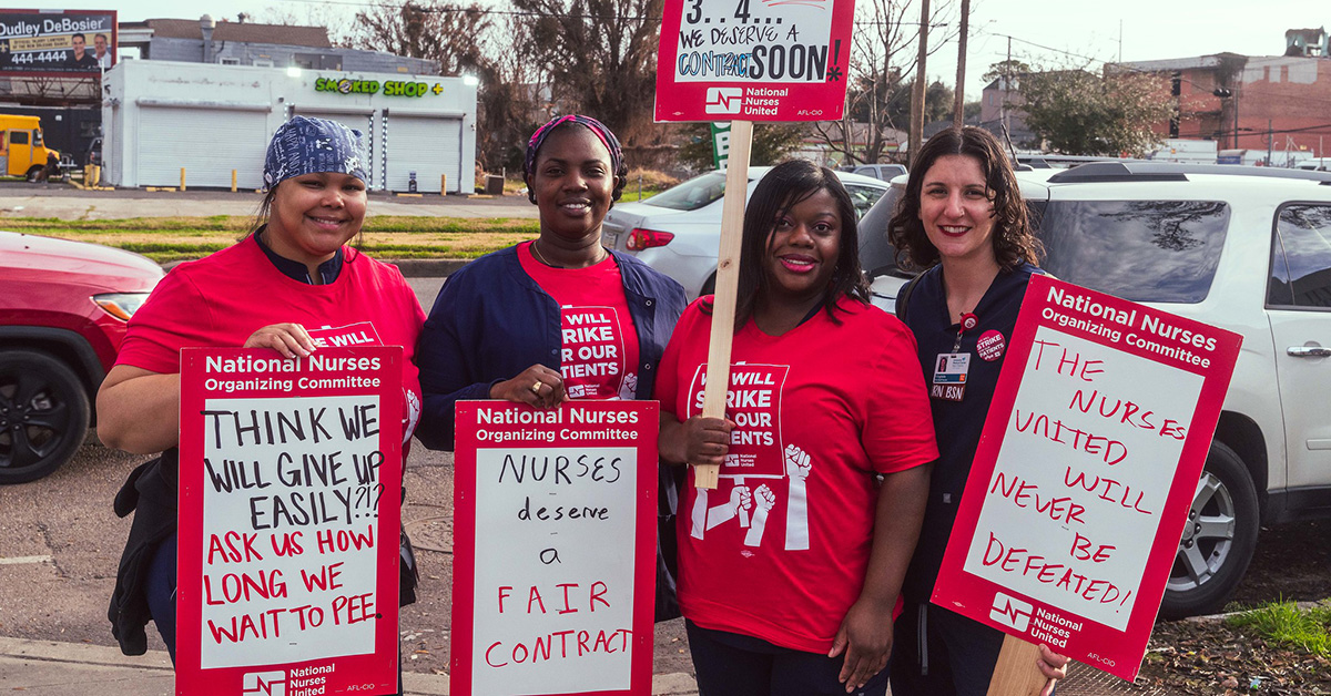 Four nurses standing outside smiling, holding signs calling for a fair contract