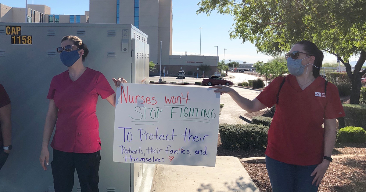 Nurses outside hold sign "Nurses won't stop fighting to protect their patients"