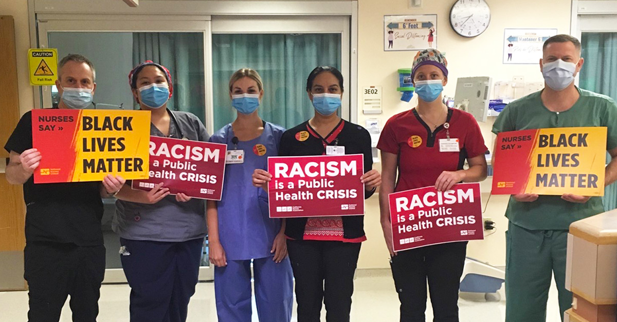 Nurses inside hospital hold signs "Racism is a Public Health Crisis" and "Nurses Say: Black Lives Matter"