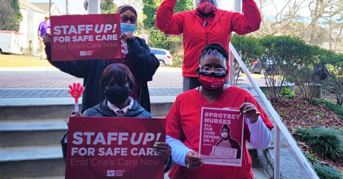 Three nurses outside with raised fists hold signs "Staff Up for Safe Care"