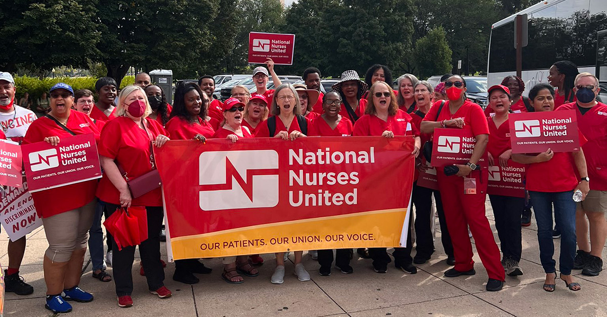 Large group of nurses holding "National Nurses United" banner in front of Washington Mounument