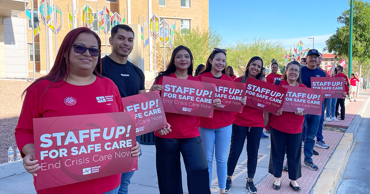 Group of four nurses outside hospital hold signs "Staff up for safe patient care"