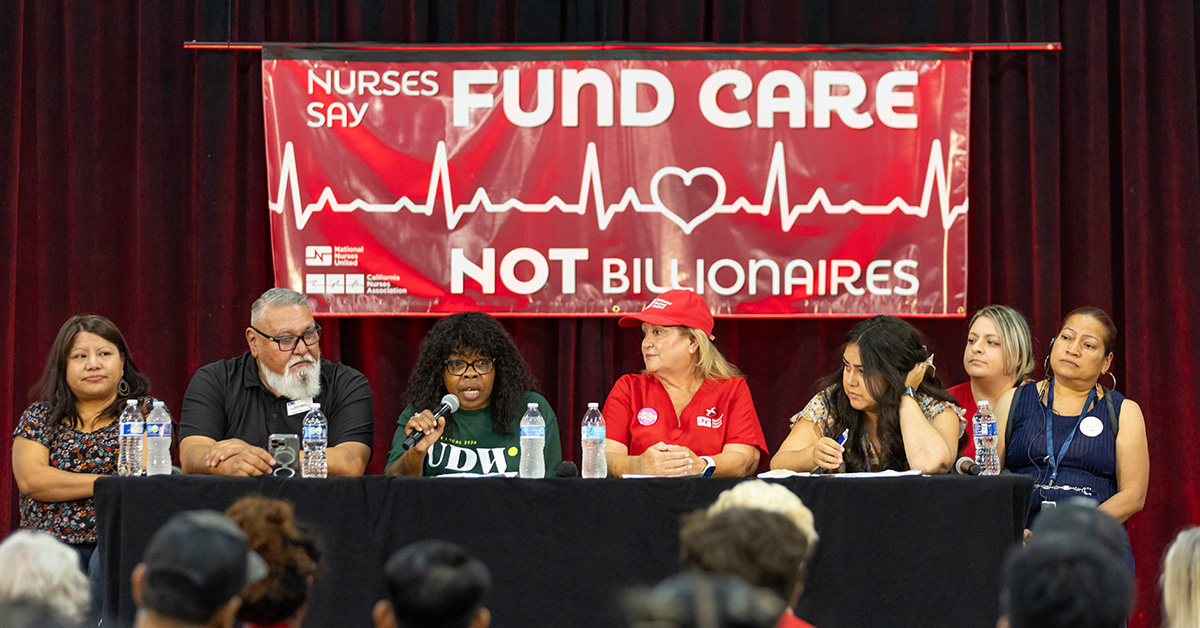 Panel at town hall in front of banner "Fund Care Not Billionaires"