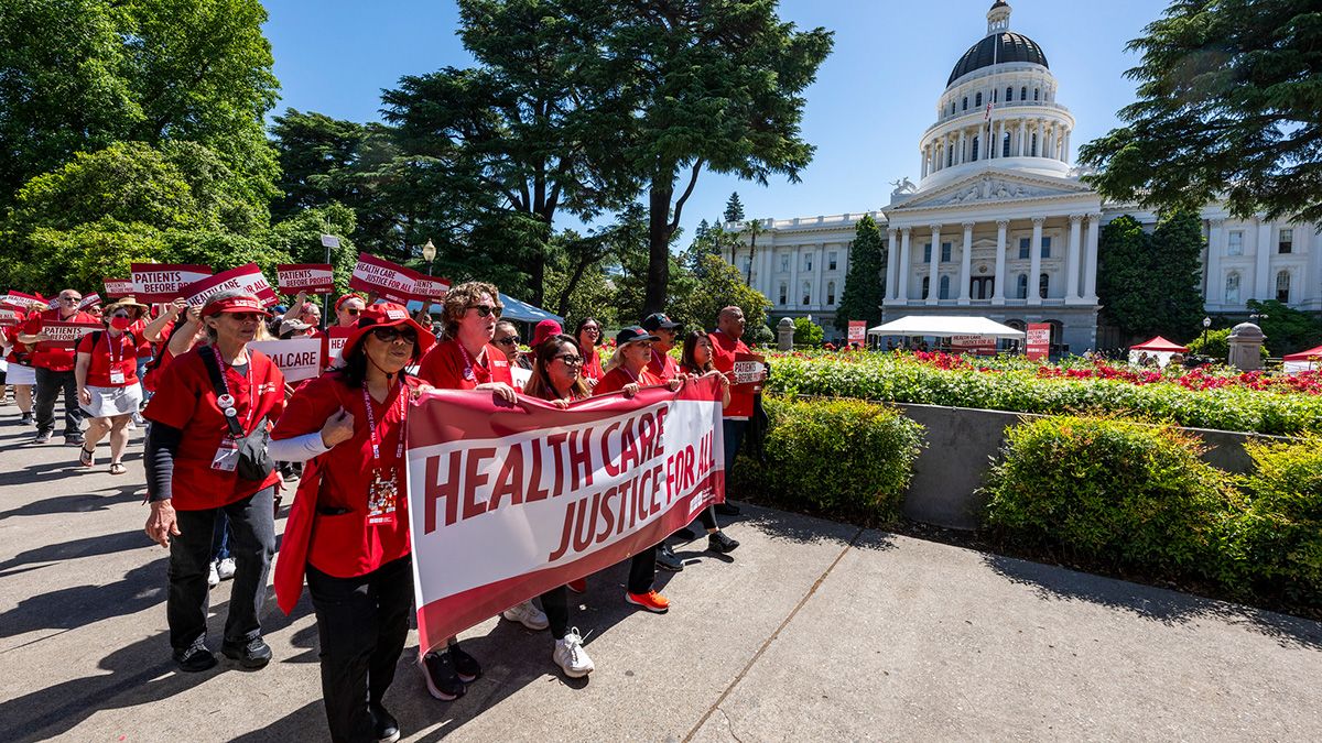 Nurses marching in front of California Capitol building holding banner "Health Care Justice for All"