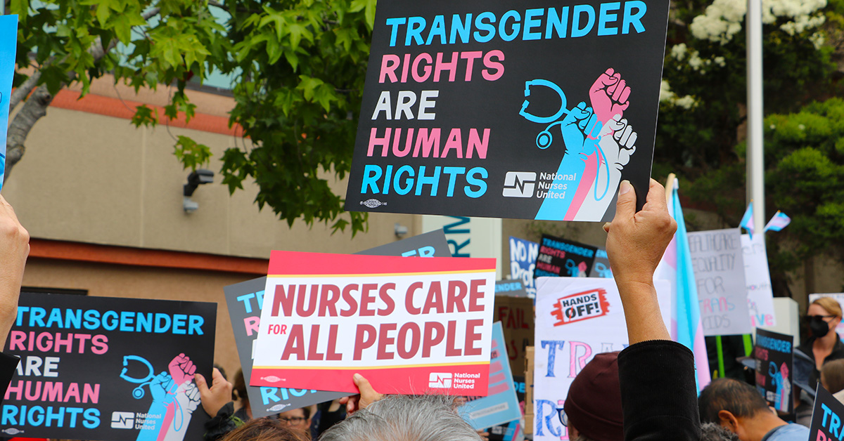 Hands holding signs "Transgender Rights Are Human Rights" and "Nurses Care for All People"