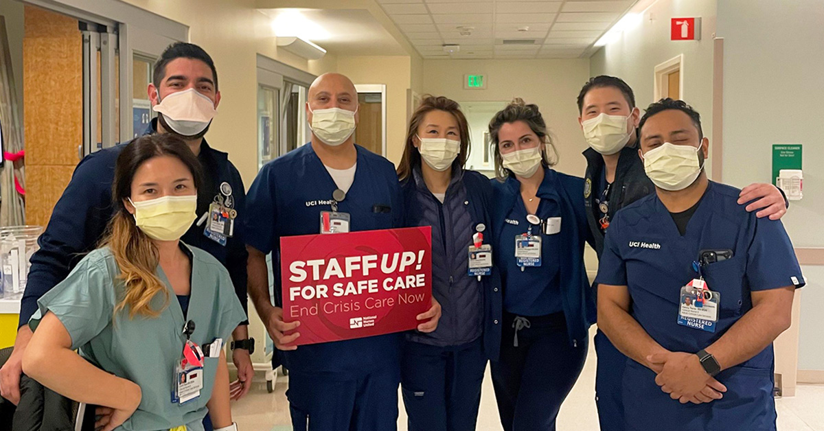 Goup of nurses inside hospital, one holds sign "Staff Up for Safe Care"