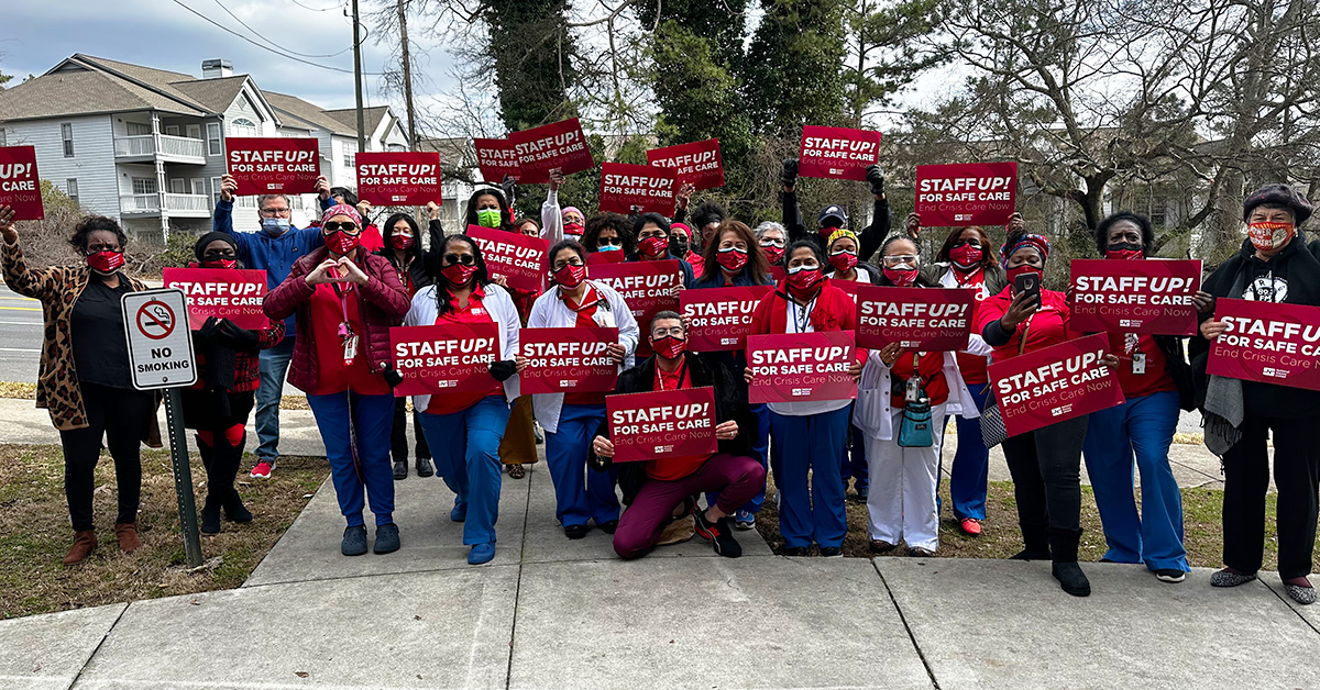 Large group of nurses outside holding signs "Staff Up for Safe Care"