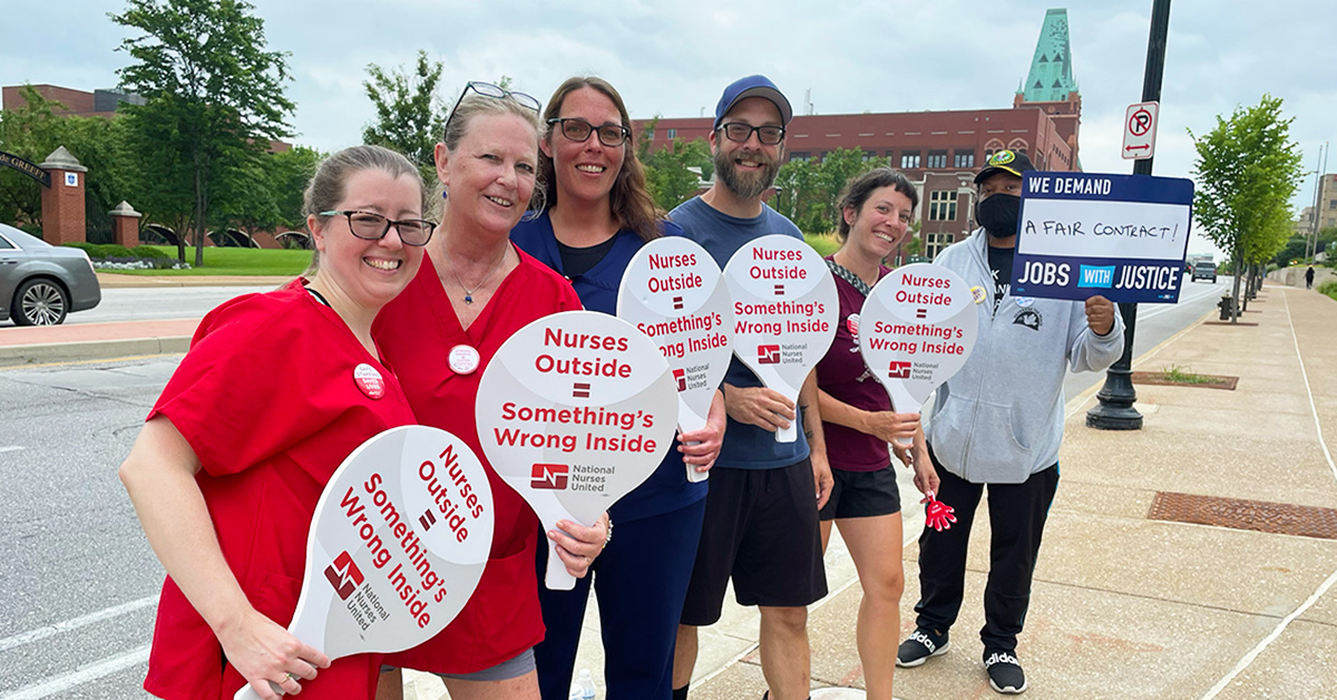 Group of nurses outside holding signs "Nurses Outside = Somethings Wrong Inside"