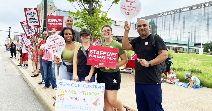 Nurses in front of Saint Louis University Hospital holding signs like "Staff up for safe care!"