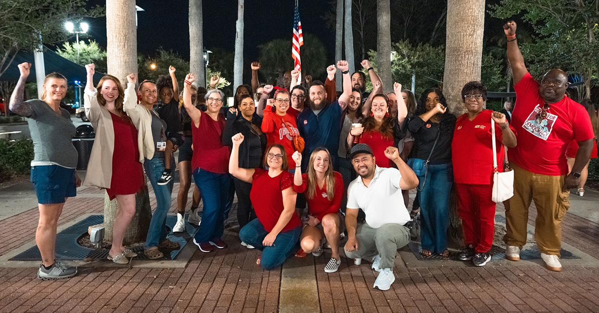 Large group of nurses outside, smiling, with raised fists