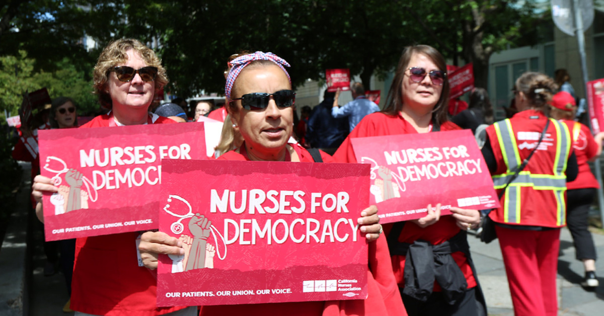 3 nurses marching, holding signs "Nurses for Democracy"