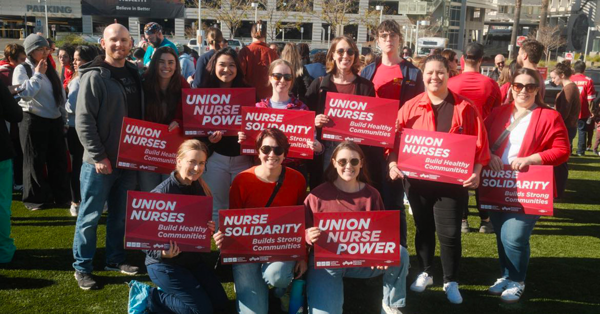 Group of nurses outside, smiling, holding signs "Union Nurse Power"