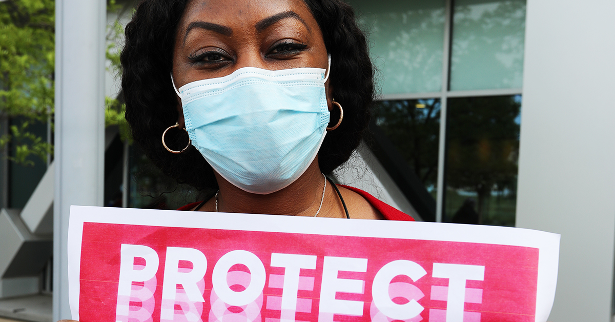 Nurse in mask holding sign: "PROTECT"