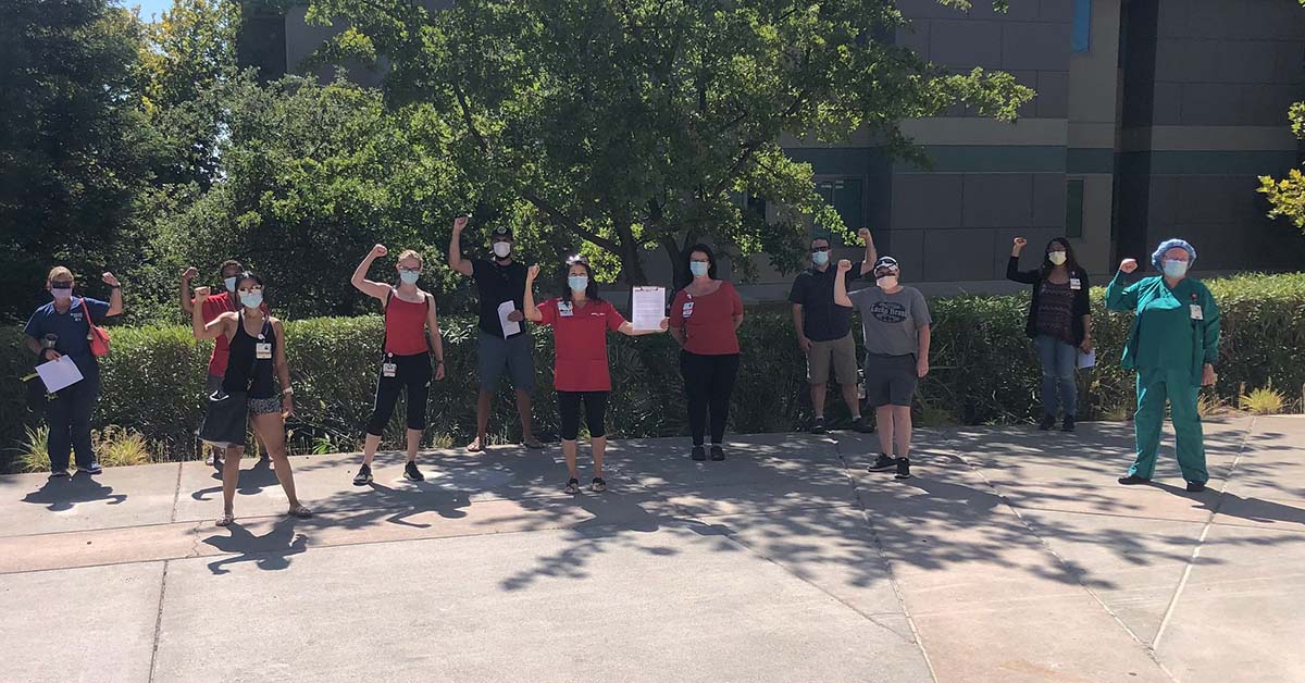 Large group of nurses outside hospital with fists raised