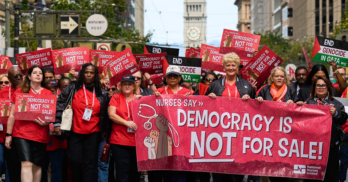 Large group of nurses marching, holding banner "Democracy is NOT for Sale"