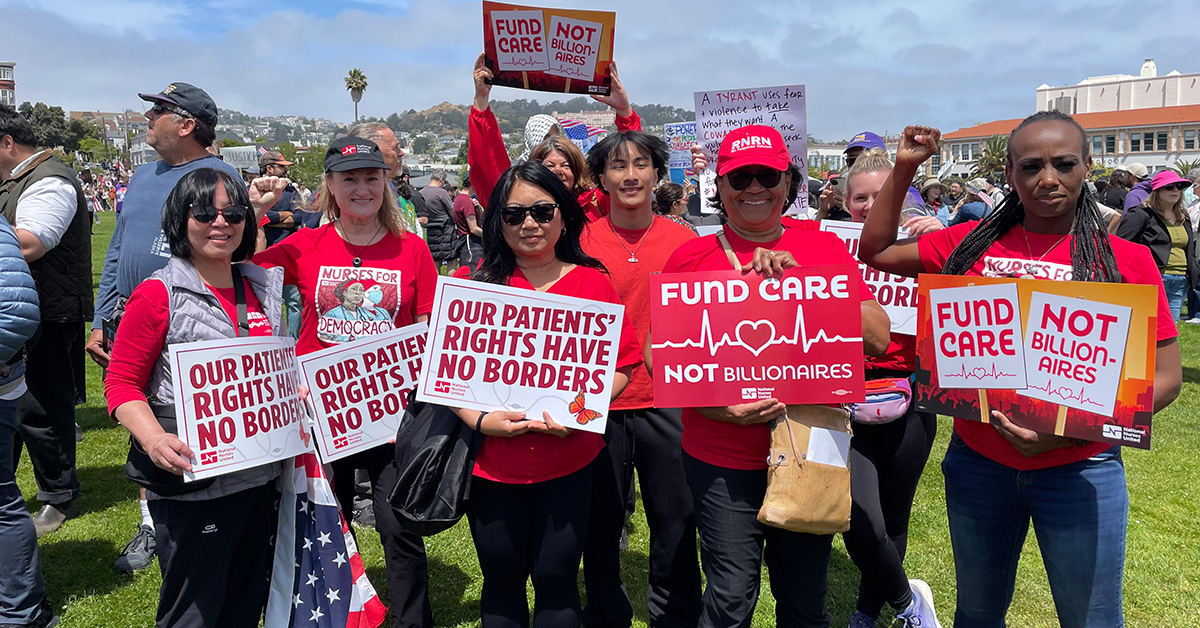 Group of nurses outside, holding signs "Our Patients Rights Have No Borders"