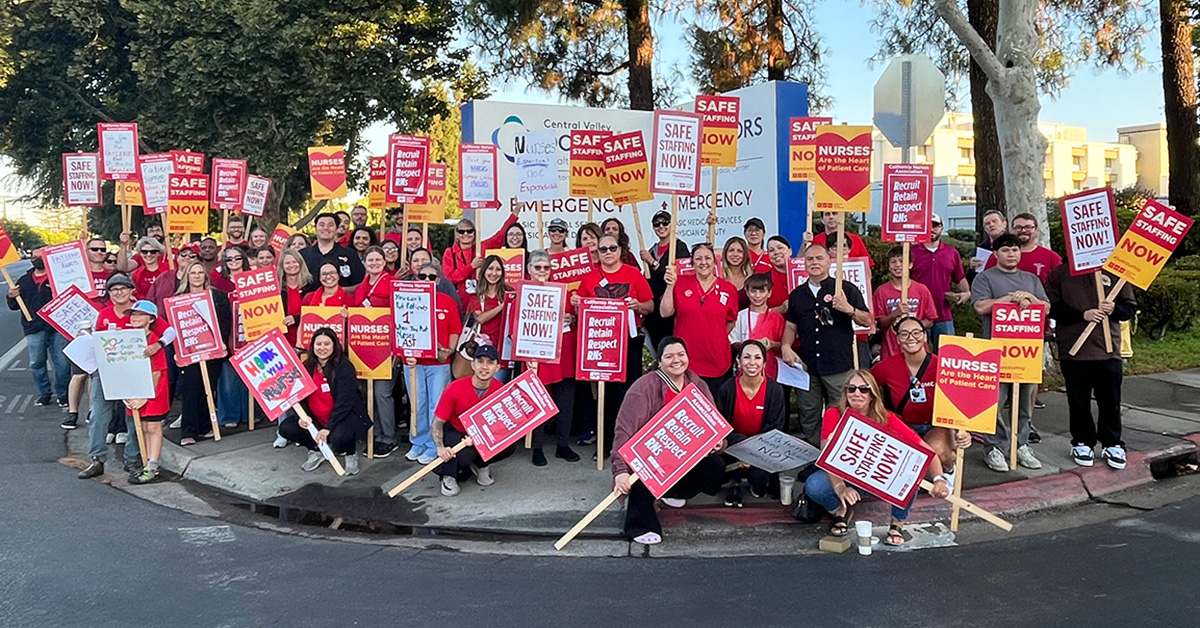 Large group of nurses outside hospital holding signs calling for safe staffing