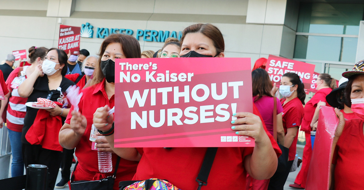 Nurse outside holds sign "There's no Kaiser without nurses"