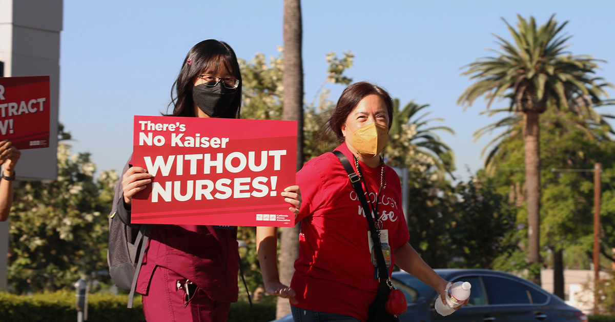 Two nurses outside, one holds sign "There's No Kaiser Without Nurses"