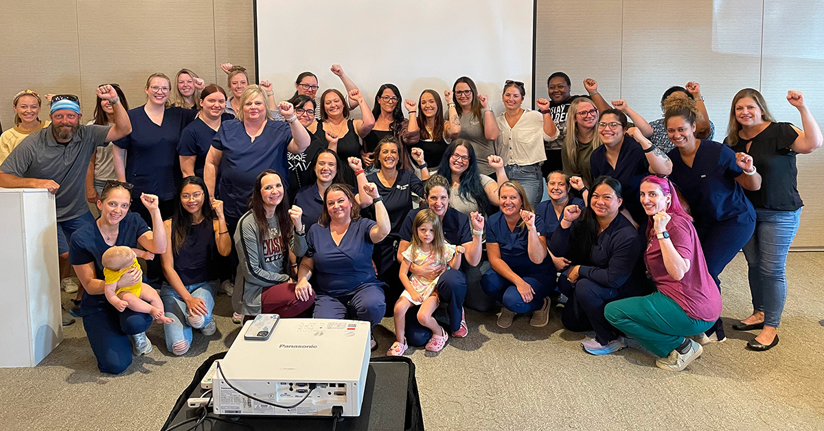 Large group of nurses inside, smiling, with raised fists