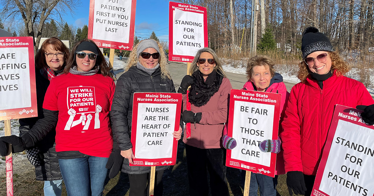 Group of nurses outside dressed in winter clothes, holding signs "Standing for our patients", "Nurses are the heart of patient care", more