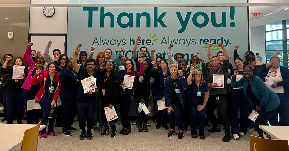 Large group of nurses inside hospital smiling, with raised fists