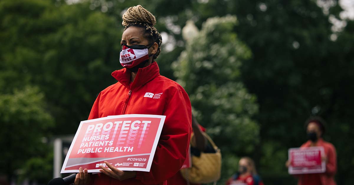 Masked nurse outside holds signs "Protect Nurses, Patients, Public Health"