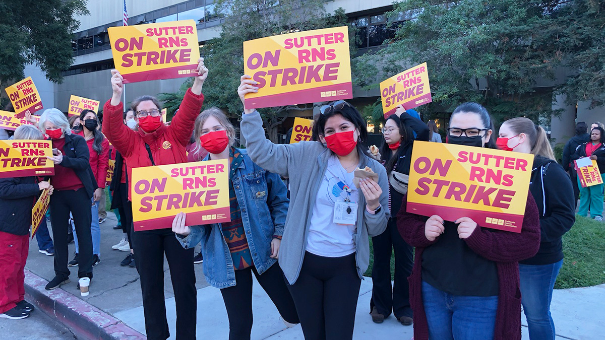 Group of nurses outside hold signs "Sutter RNs on Strike"