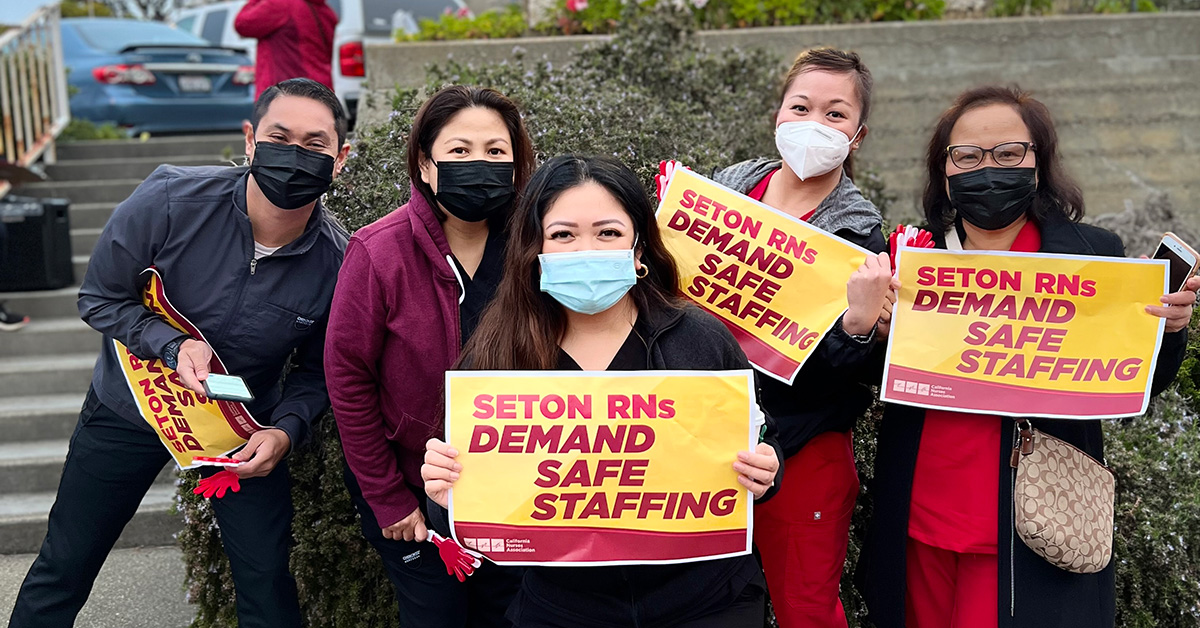 Group of five nurses outside Seton Medical Center, holding signs "Seton RNs Demand Safe Staffing"