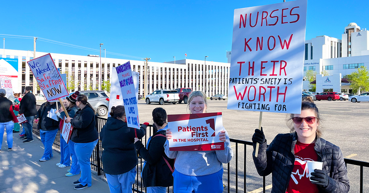 Nurses picketing outside hospital hold signs calling for patient safety and safe staffing