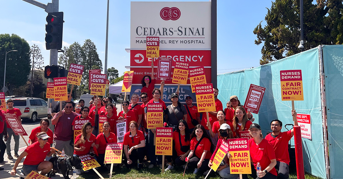 Nurses holding signs in front of Cedars-Sinai "Some cuts don't heal" and "Nurses demand a fair contract now"