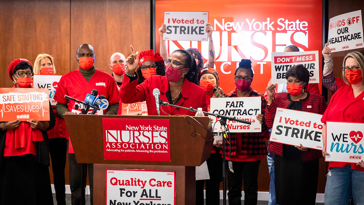 Nancy Hagan at podium backed by nurses holding various signs