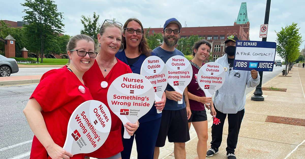 Group of nurses outside hospital hold signs "Nurses Outside = Something's Wrong Inside"