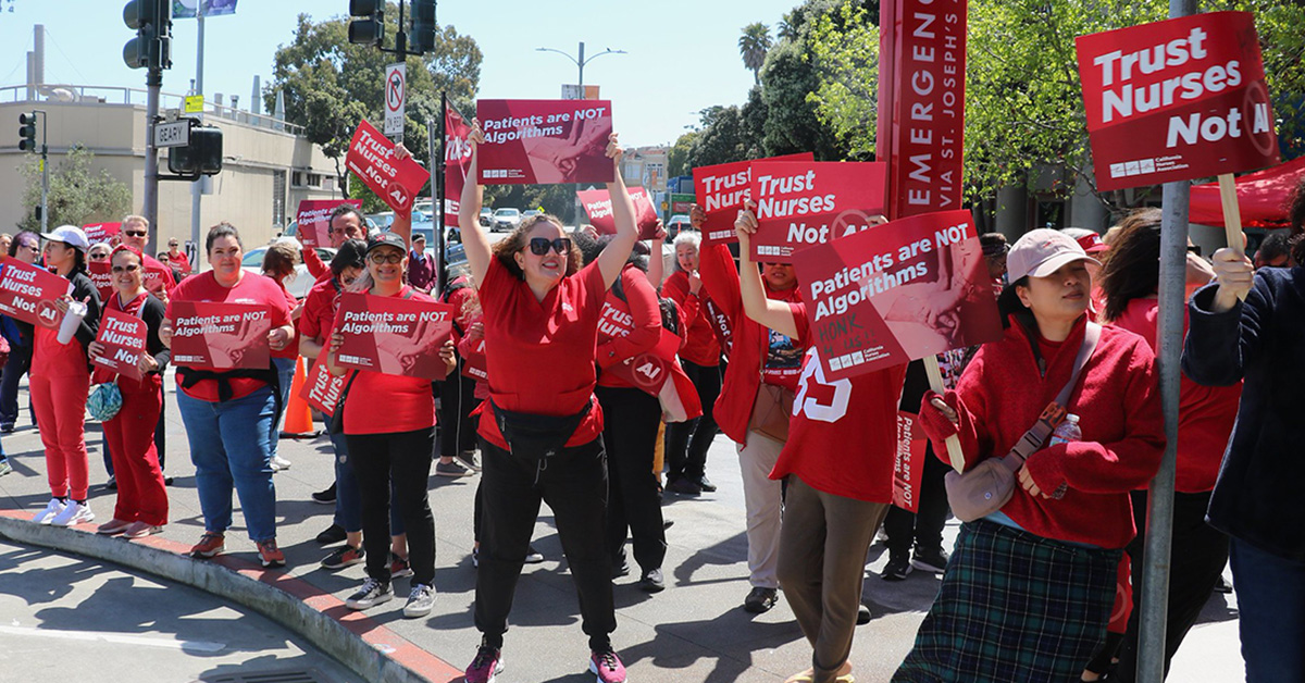 Nurses picketing outside hospital, holding signs "Patients are not algrorithms"