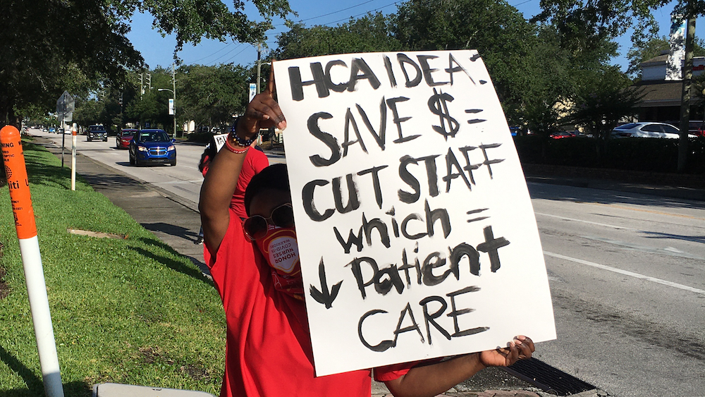 Nurse holds sign protesting HCA cost cutting measures