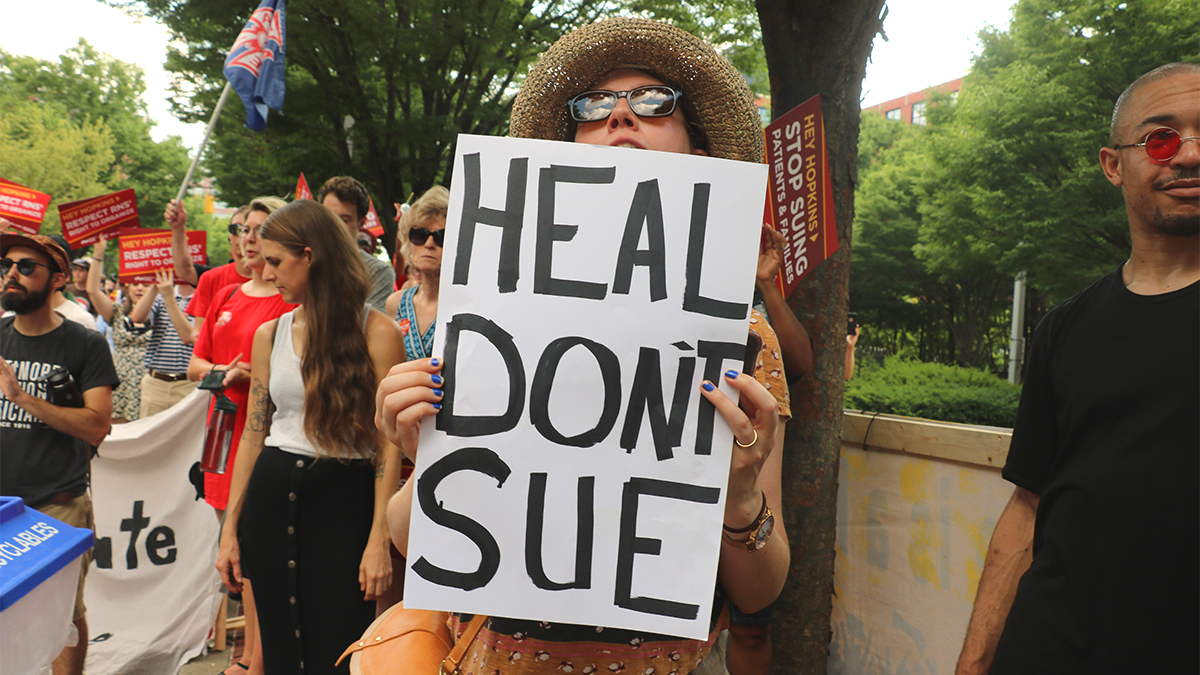 Woman holds sign "Heal Don't Sue"