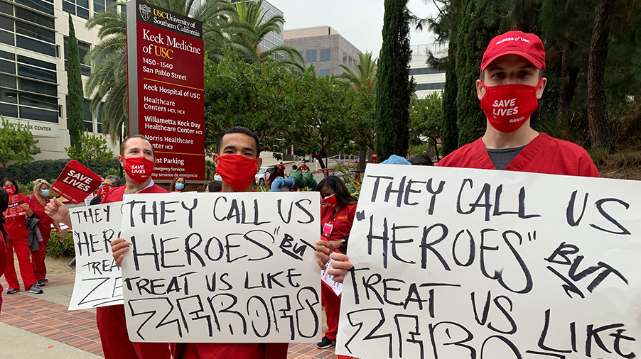 Nurses hold signs "They call us heroes but treat us like zeroes"