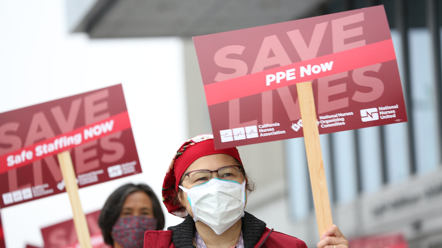 Nurse holds sign "Save Lives, PPE Now"