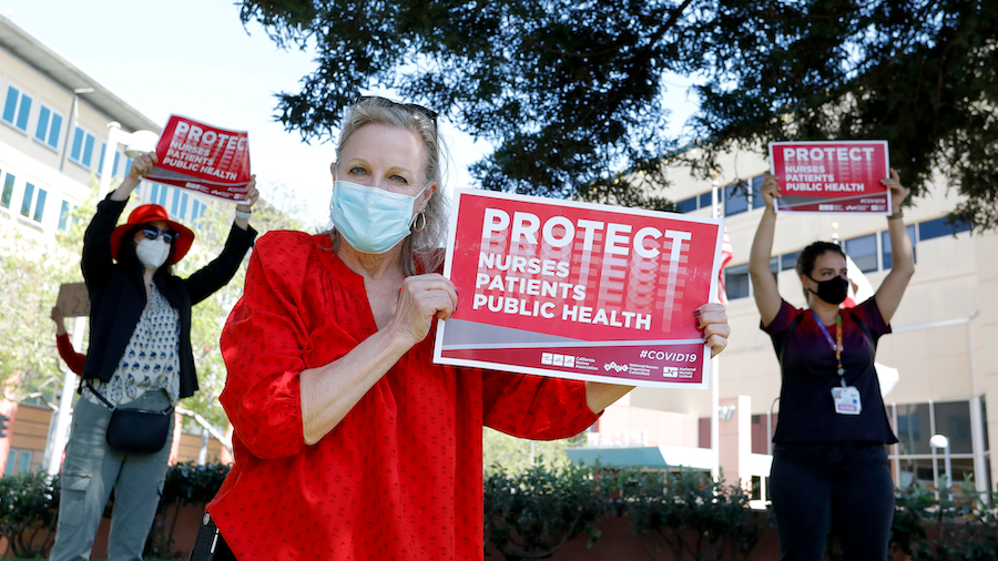 Nurse holds sign "Protect Nurses, Patients, Public Health"