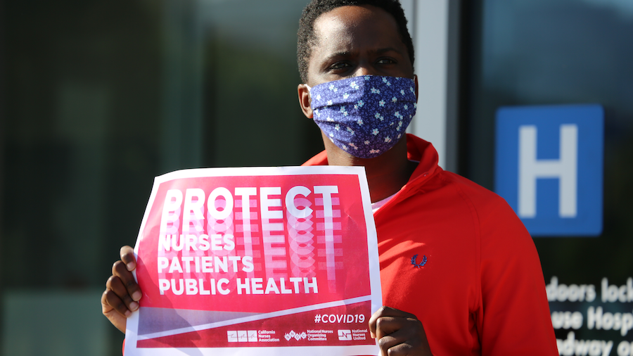 Nurse holds sign "Protect Nurses, Patients, Public Health"