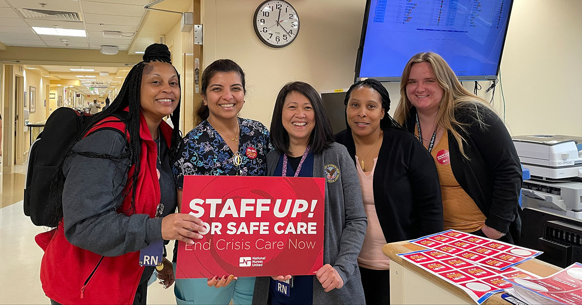 Five nurses inside hospital hold signs "Staff Up for Safe Patient Care"
