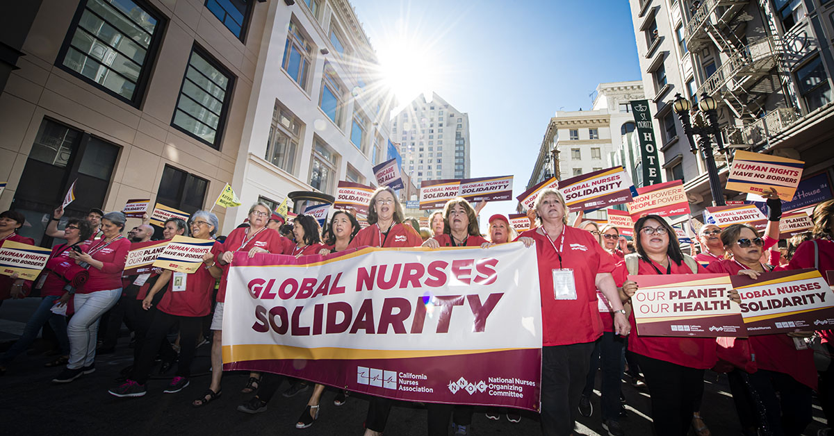 Nurses marching, holding banner that reads "Global Nurses Solidarity" and sign that reads "Our Planet, Our Health"