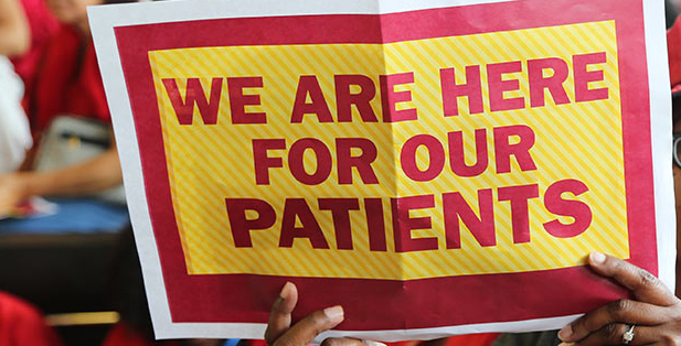 Nurse holding up sign that reads "We are here for our patients."