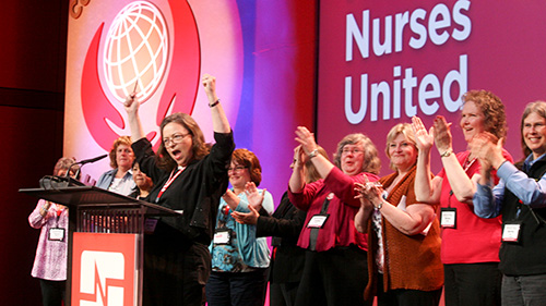 Nurses standing in front of convention podium with hands raised in celebration.