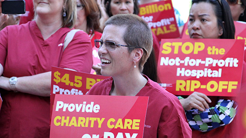 Nurse holds sign "Provide charity care or pay"