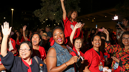 Large group of nurses celebrating outside with hands raised