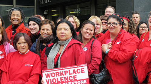 Nurse stand outside building holding signs "Workplace violence effects everyone"