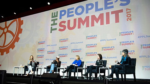 Panel sits in front of large banner "The People's Summit"