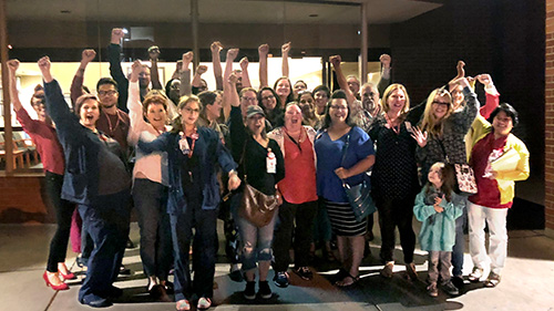Large group of nurses outside hospital celebrating with raised fists