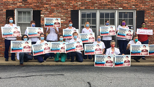 Group of nurses outside hold signs "Asheville Community Support Mission Nurses"